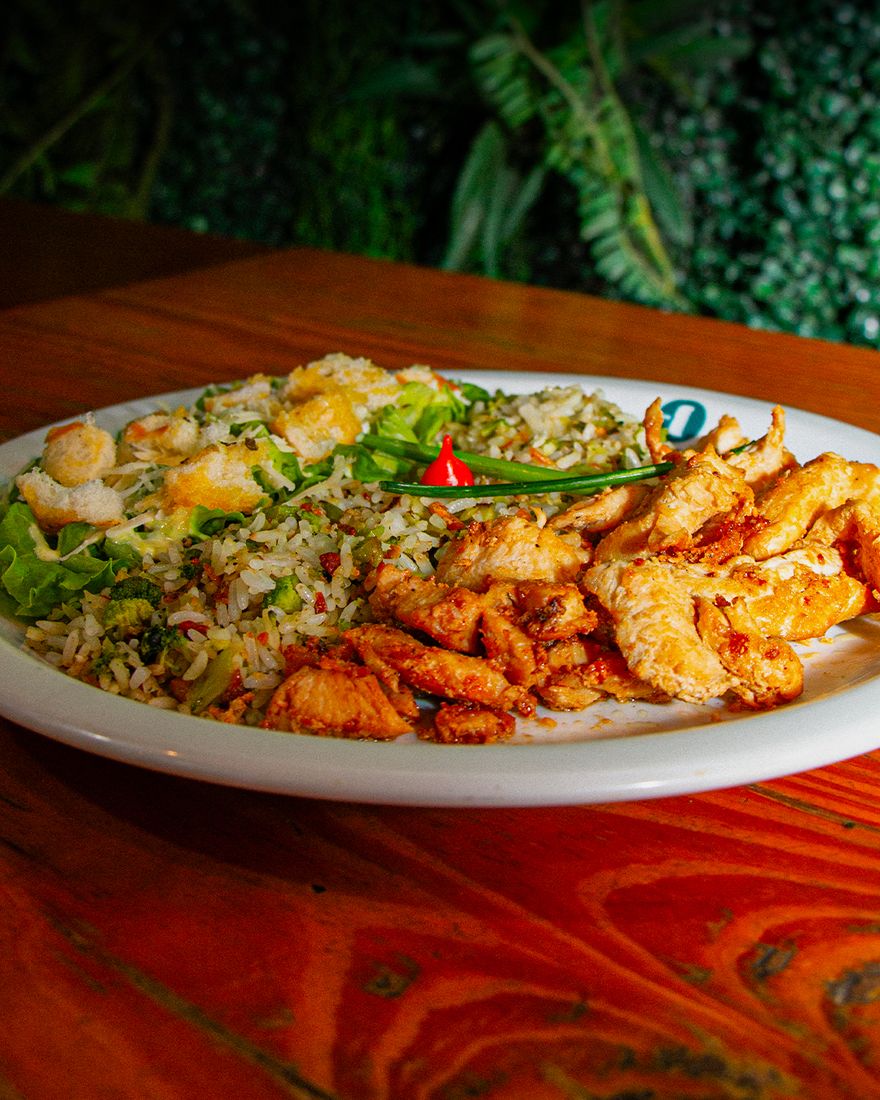 Prato de frango com arroz de brócolis e salada Caesar sobre a mesa de madeira do Berton